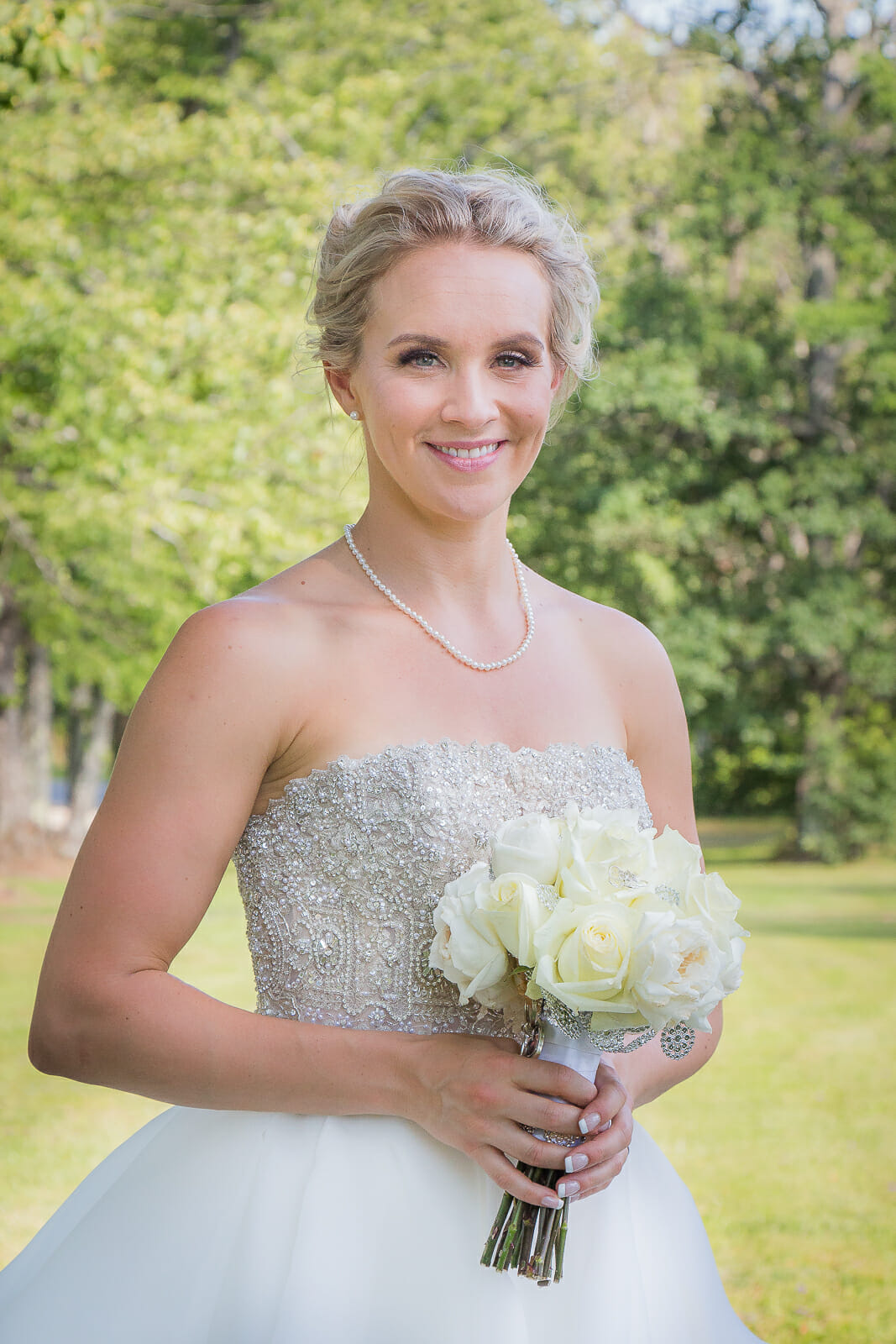a beautiful bride holding her white rose bouquet looking and smiling right at the camera.